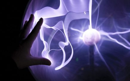 closeup photo of a hand touching a purple plasma lamp